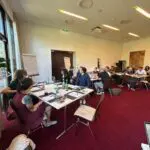 Menschen in einem Raum mit Tischen und Stühlen