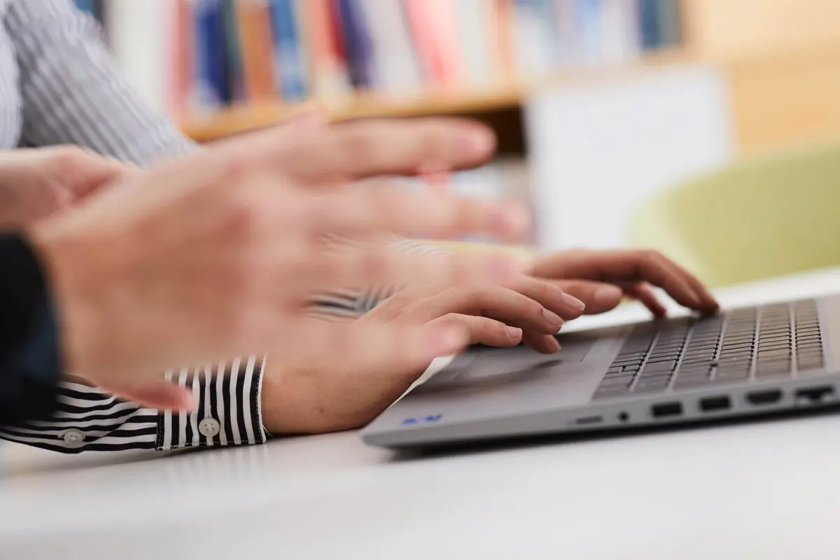 Zwei Hände verschwommen vorne und zwei Hände auf einer Laptoptastatur.